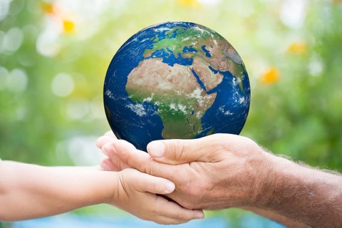 Child and senior man holding planet Earth in hands against green spring background. Elements of