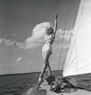1940s sailing boat. A young woman is aboard a fashionable sailing boat and is standing on deck when