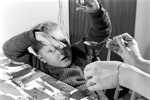 A boy is sick and won't take his medicine. His mother holds out a spoon and waits for him to gape