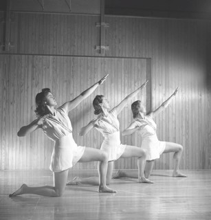 Gymnastics in the 1940s. Three young female gymnasts are practicing together and doing the same