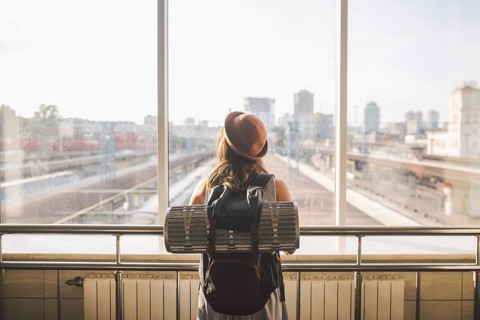 Traveler Rear view woman standing at the window in hall Train Station departure with backpack,