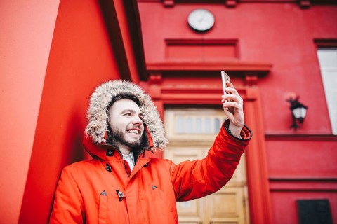 Handsome young male student with smile and beard stands on background red wall, facade of