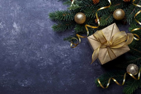 Christmas flat lay with golden gift box and fir tree branch on black stone background with copy