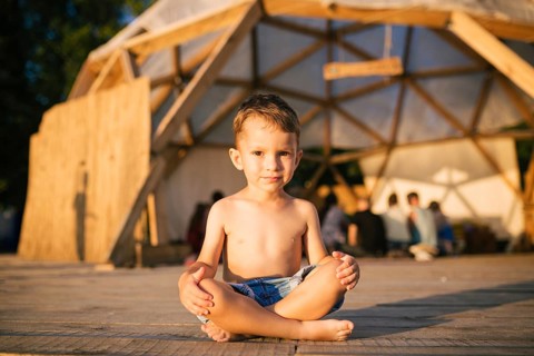 Theme is yoga and children. Caucasian Boy child sitting barefoot cross-legged in lotus position on