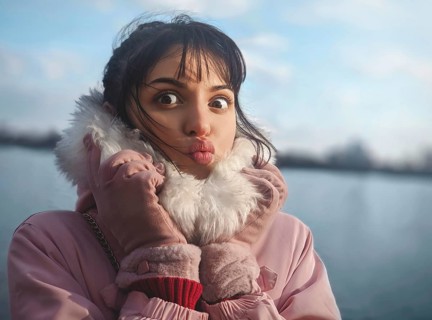 Portrait of a cute lady with a kiss, with bangs, in a pink jacket on the background of the river