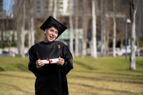 Young gay man recent graduated, dressed in cap and gown, showing off his degree celebrating