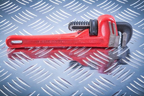 Monkey wrench on channeled metal background construction concept