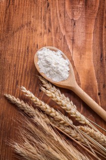 Wooden spoon with white flour and ears of wheat rie on vintage board