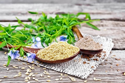 Flax bran and flour in two spoons on a burlap napkin, linen leaves and flowers on a wooden board