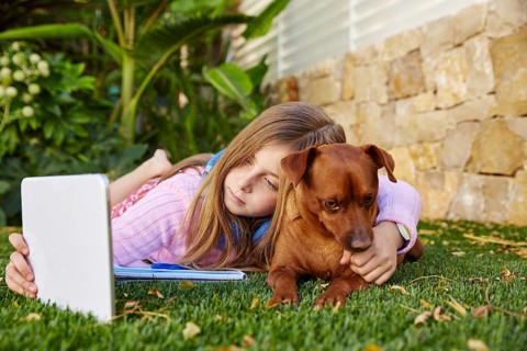Blond kid girl selfie photo with tablet pc and dog lying on grass