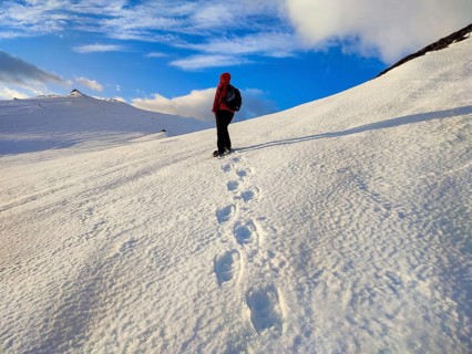 Person walking over snow-covered mountains, clear skies and footprints in the snow, Tromsø, Norway,