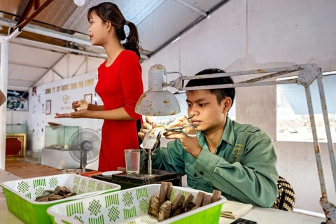 A man concentrates on his work while a woman stands next to him, pearl farm in Halong Bay, Vietnam,