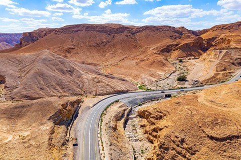 Asphalt highway meanders among the hills. Dead Sea mud has healing properties. Drone filming.
