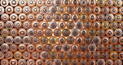 Multiple used AA alkaline batteries are seen arranged in a pile. Closeup front view from the plus