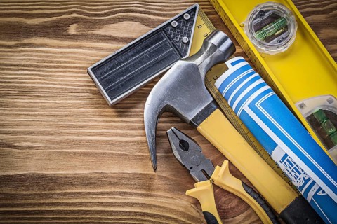 Blue blueprints construction level try square claw hammer pliers on wooden board