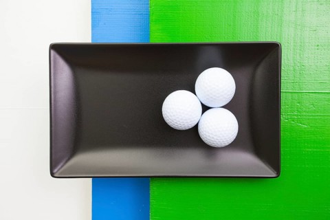 Black ceramic dish with golf balls on over white, blue and green wooden table, rectangle dish