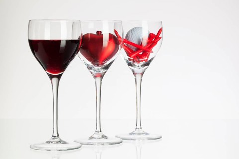 Wine glasses with red wine, heart and golf ball on white table
