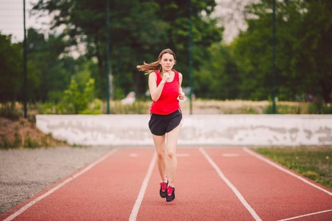 Beautiful young athlete Caucasian woman with big breasts in red T-shirt and short shorts running