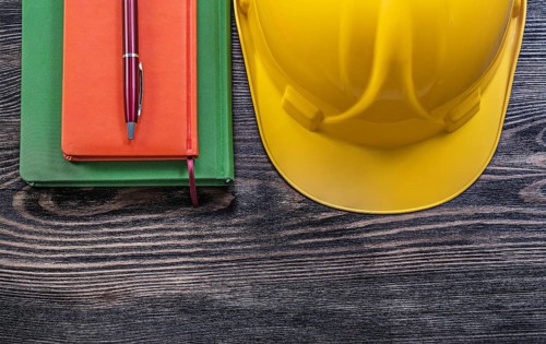 Note-books ballpoint pen protective building helmet on wooden board construction concept