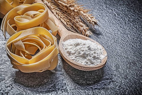 Wheat rye ears wooden spoon flour raw twisted Italian pasta on black background