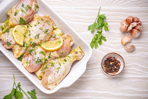 Raw uncooked chicken legs marinated with seasonings, herbs, lemon in white ceramic casserole top