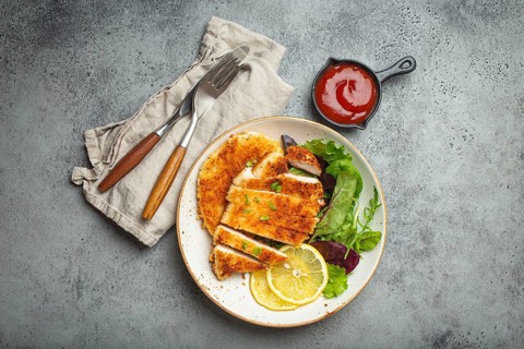 Crispy panko breaded fried chicken fillet with green salad and lemon cut on plate on gray rustic