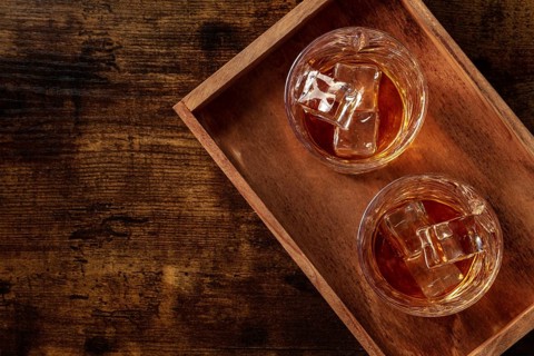 Whiskey in glasses with ice. Bourbon whisky on rocks on a dark rustic wooden background, overhead