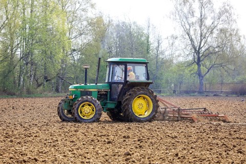 Farmer cultivating field with green John Deere 2140 utility tractor and harrow in the spring. Salo,