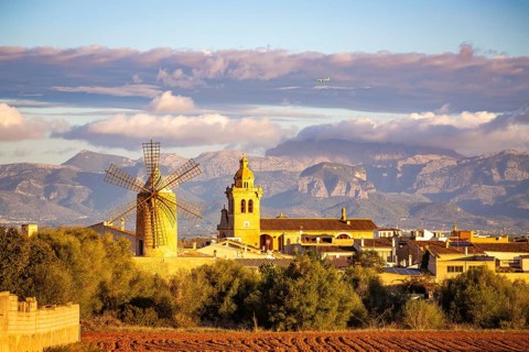 Mountain landscape with village, windmill and church tower under a cloudy sky and flying aeroplane