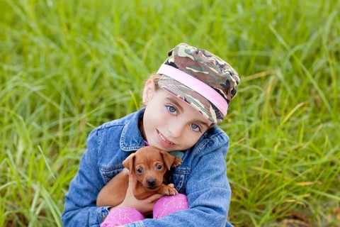 Little girl with pet puppy mascot mini pinscher in outdoor green grass