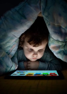 Little girl watching her tablet in the bed. Illuminated child face from device screen. Child