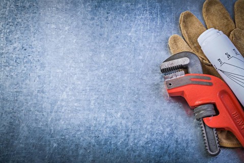 Monkey adjustable wrench protective gloves rolled blueprints on metallic background plumbing