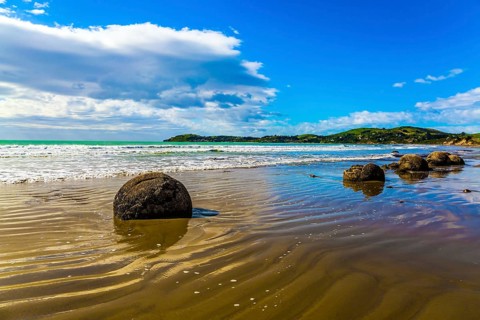 Moeraki's huge round boulders on a sandy beach. The Pacific ocean tide begins in New Zealand. The