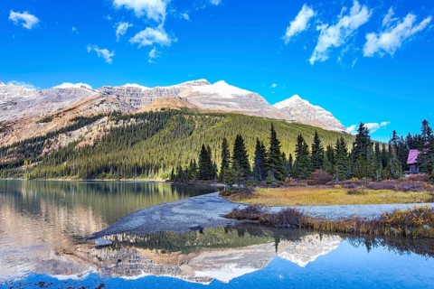Canada. Rocky Mountains. Sun and mountains are reflected in the smooth water of the lake. Glacial