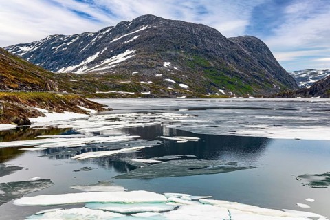 Norway. The cold clear water of the lake Djupvatnet is covered with ice in July. The mountains are
