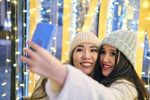 Two girlfriends asian girls in white coats are having fun hugging and selfie on mobile phone, new