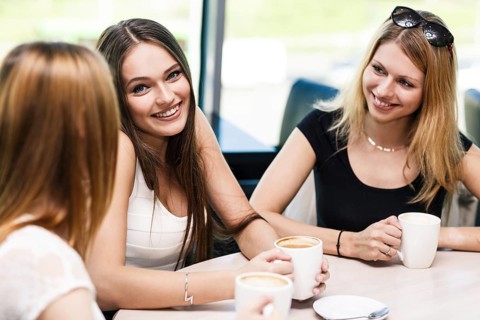 Happy women holding coffee cup while looking at each other in cafe