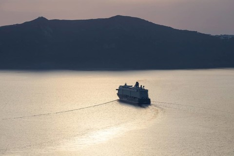 Golden evening light, view from Fira, cruise ship leaving Santorini archipelago, Thirassia island