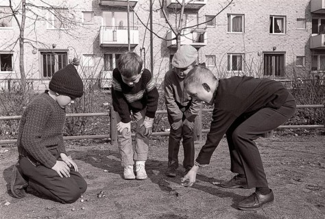 In the 1960s. Boys outdoors playing marbles. An old fashioned game where the goal is to hit the
