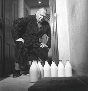 Man of the 1940s. A man visibly disapointed over the several milk bottles standing on his doorstep.