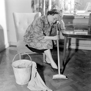 Cleaning the floor back then. A woman looks very tired and worn out when sitting on a chair, having
