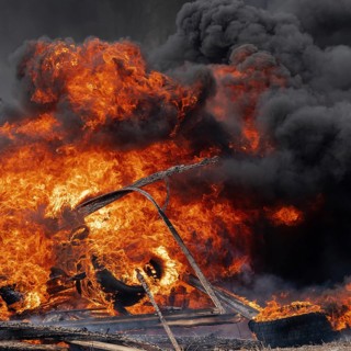 Burning cars tires, strong flame of red-orange fire and clouds of black smoke in sky. Selective