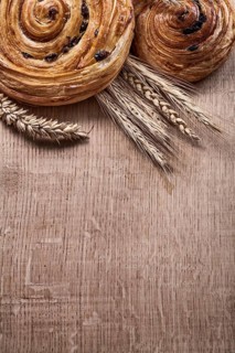 Golden wheat ears raisin baked buns on oaken wooden board food and drink concept