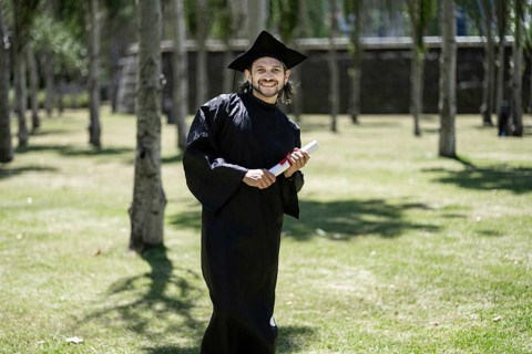 Portrait, student and happy man at graduation with certificate in university campus for success and