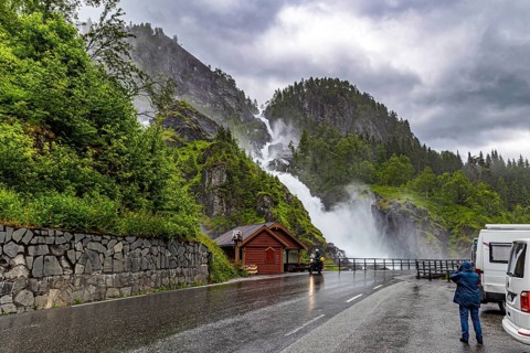 Woman tourist taking pictures of scenic double waterfall Lotefossen. Summer rainy day. The road