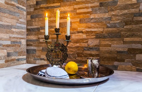Beautiful candlestick with burning candles, a silver glass for blessing and a white yarmulke.
