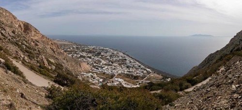 View down to serpentine road and Kamari at the lava beach, in the sea the island Anafi, panoramic