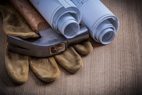 Rolled blueprints protective gloves and claw hammer on wooden board