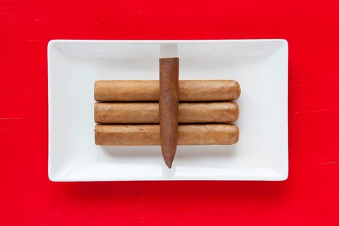 White ceramic dish with luxury Cuban cigars on over red background, rectangle dish