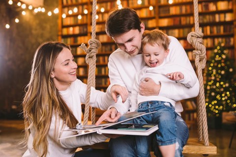 Family With Baby Relaxing On home Swing Seat in cozy dark living room on Christmas eve. Family